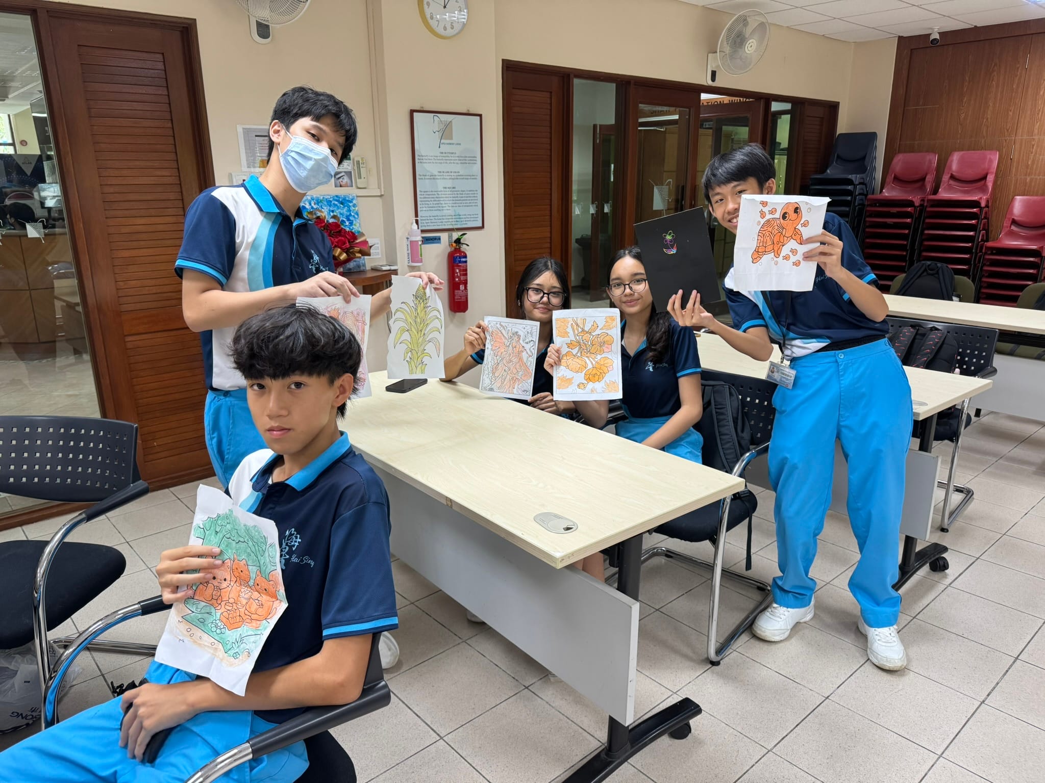 Students in school uniform smiling and displaying their colorful drawings and artwork during a class activity.